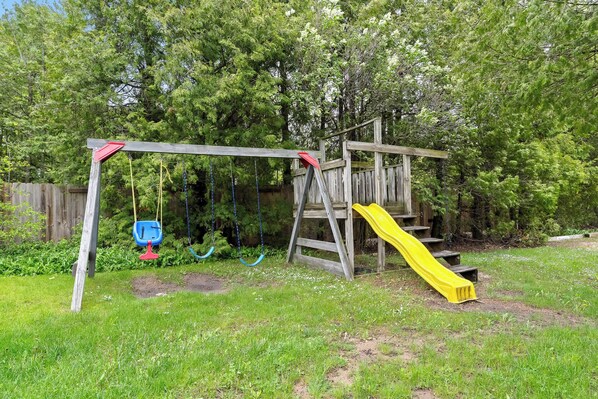Una estructura de juego de madera con un tobogán y columpios en un patio cubierto de césped.
