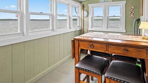 Een kamer met een houten bureau, twee leren stoelen en uitzicht op het water door grote ramen.