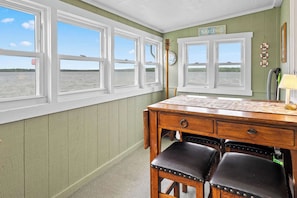 A room with a wooden desk, two leather chairs, and a view of the water through large windows.