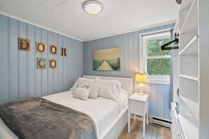 A bedroom with a bed, a nightstand, a window, and wall decorations. - Blue Sky Cottage: Sunset Shores Kangaroo Lake (Baileys Harbor)