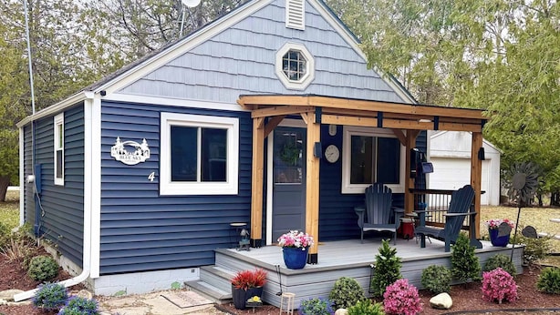 A single-story house with a porch, a small deck, and a variety of potted plants.