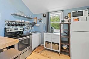 A compact kitchen with a stove, oven, and microwave, a window with a view, and a small refrigerator.