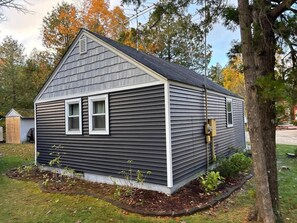A single-story house with a gabled roof, a front porch, and a small front yard with a tree and shrubs. - Blue Sky Cottage: Sunset Shores Kangaroo Lake (Baileys Harbor)