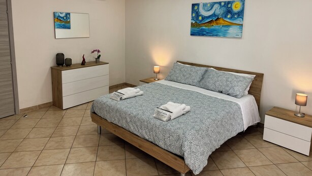 A bedroom with a bed, bedside tables, a dresser, an air conditioning unit, and artwork on the walls. - Andrea's Place - cozy apartment 5 minutes from the Archaeological Museum (Napoli)