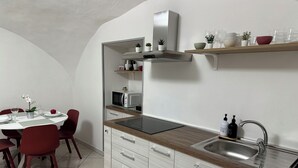 A modern kitchen with a built-in microwave, a stainless steel sink, and a wooden countertop. There are red chairs around a dining table with a vase of flowers. - Andrea's Place - cozy apartment 5 minutes from the Archaeological Museum (Napoli)