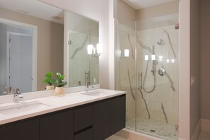 A modern bathroom with a large mirror, two sinks, dark cabinets, and a glass-enclosed shower area.