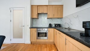A modern kitchen with wooden cabinets, a stainless steel oven, a black countertop, and a marble backsplash. - Avari Apartments – Gray’s Collection (London)