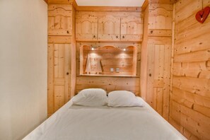 Een houten kamer met een bed, een plank met decoratieve objecten en een hartvormige decoratie aan de muur.