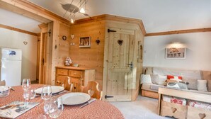 A cozy room with a wooden dining table set for four, a sofa, and a small kitchenette. - Ground floor, parking, ski locker, 45m², Les Gets (Les Gets)
