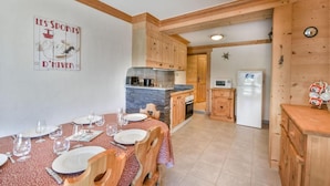 A dining area with a table set for four, wooden cabinets, a stone countertop, and a kitchen with a refrigerator and microwave. - Ground floor, parking, ski locker, 45m², Les Gets (Les Gets)