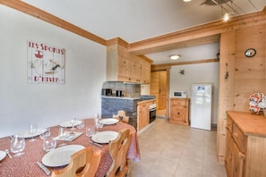 Comedor con una mesa preparada para cuatro, armarios de madera, encimera de piedra y cocina equipada con refrigerador y microondas.
