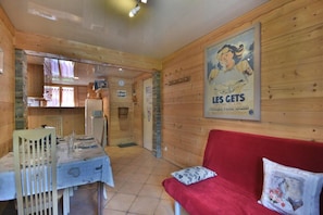 A cozy wooden interior with a dining area, a red sofa, and a poster on the wall.