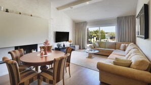 Ein modernes Wohnzimmer mit einem runden Esstisch, gestreiften Stühlen, einem beigen Sofa und einem an der Wand befestigten Flachbildfernseher.