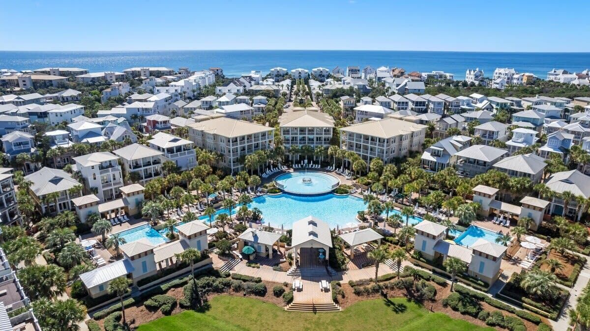 A resort with multiple buildings, a central pool, and a view of the ocean.