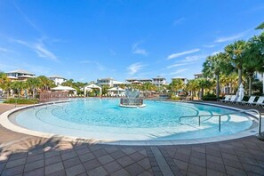 A swimming pool with a central fountain, surrounded by lounge chairs and palm trees.