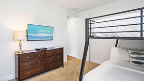 A bedroom with a bunk bed, a dresser, a flat-screen TV, and a painting.