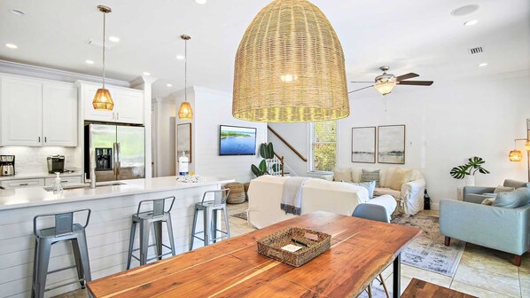 A modern kitchen with a central island, bar stools, and a dining table with a woven basket.