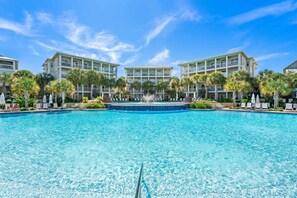 A hotel with a large pool, multiple balconies, and palm trees.