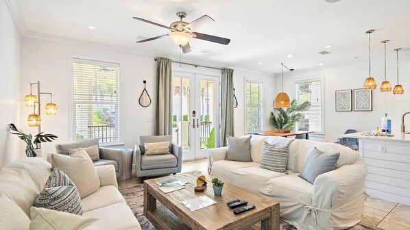 Una sala de estar moderna con ventilador de techo, comedor con mesa y sillas, y ventanas grandes con persianas.