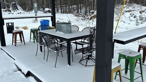 An outdoor covered patio with a table and chairs, a blue barrel, and a metal container labeled "KONIKS". - Charming luxury studio cottages with hints of rustic flare to help you RECHARGE (Woodville)