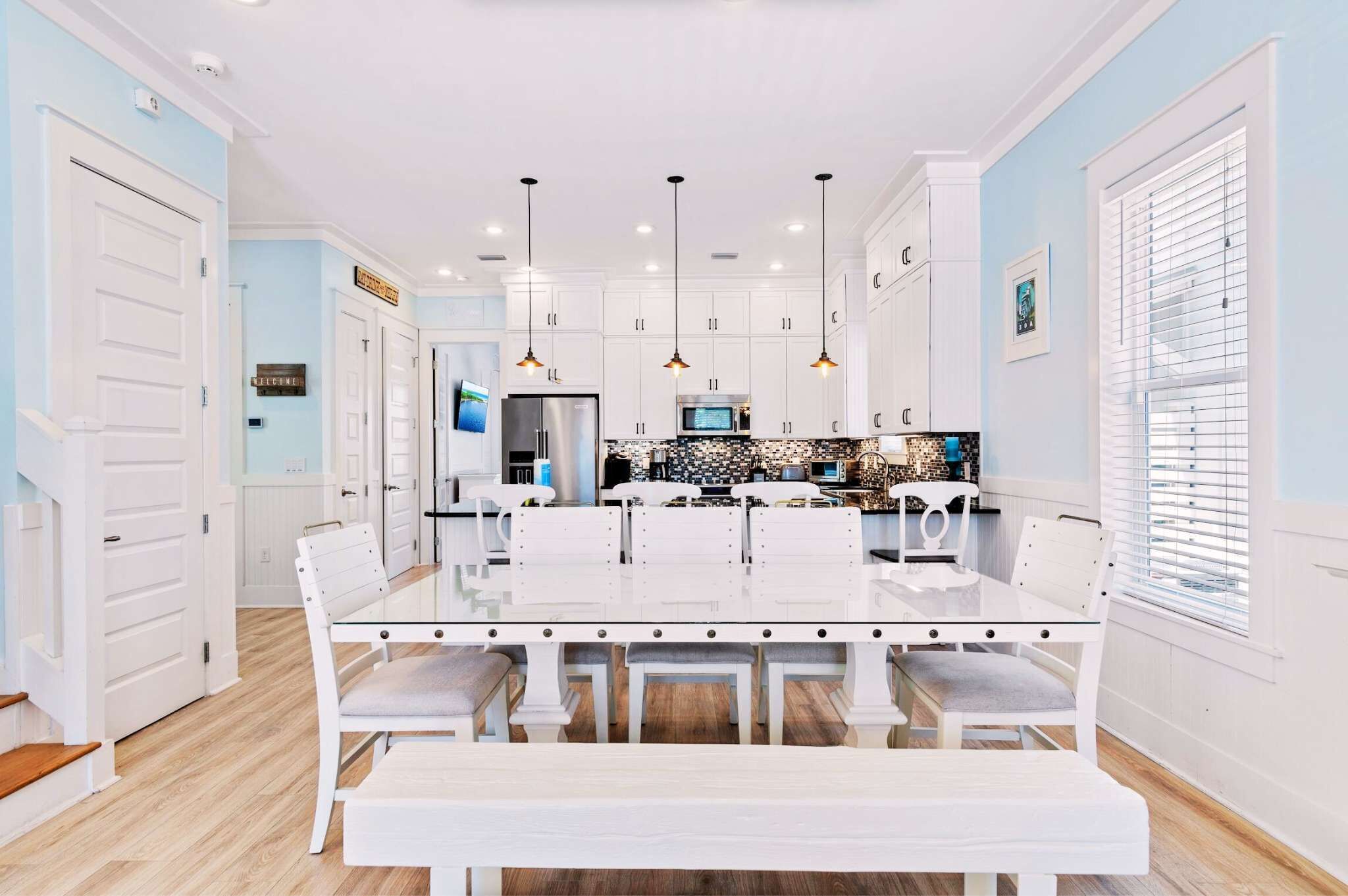 A modern kitchen with white cabinetry, a central island, pendant lighting, and a dining area with a white table and chairs.