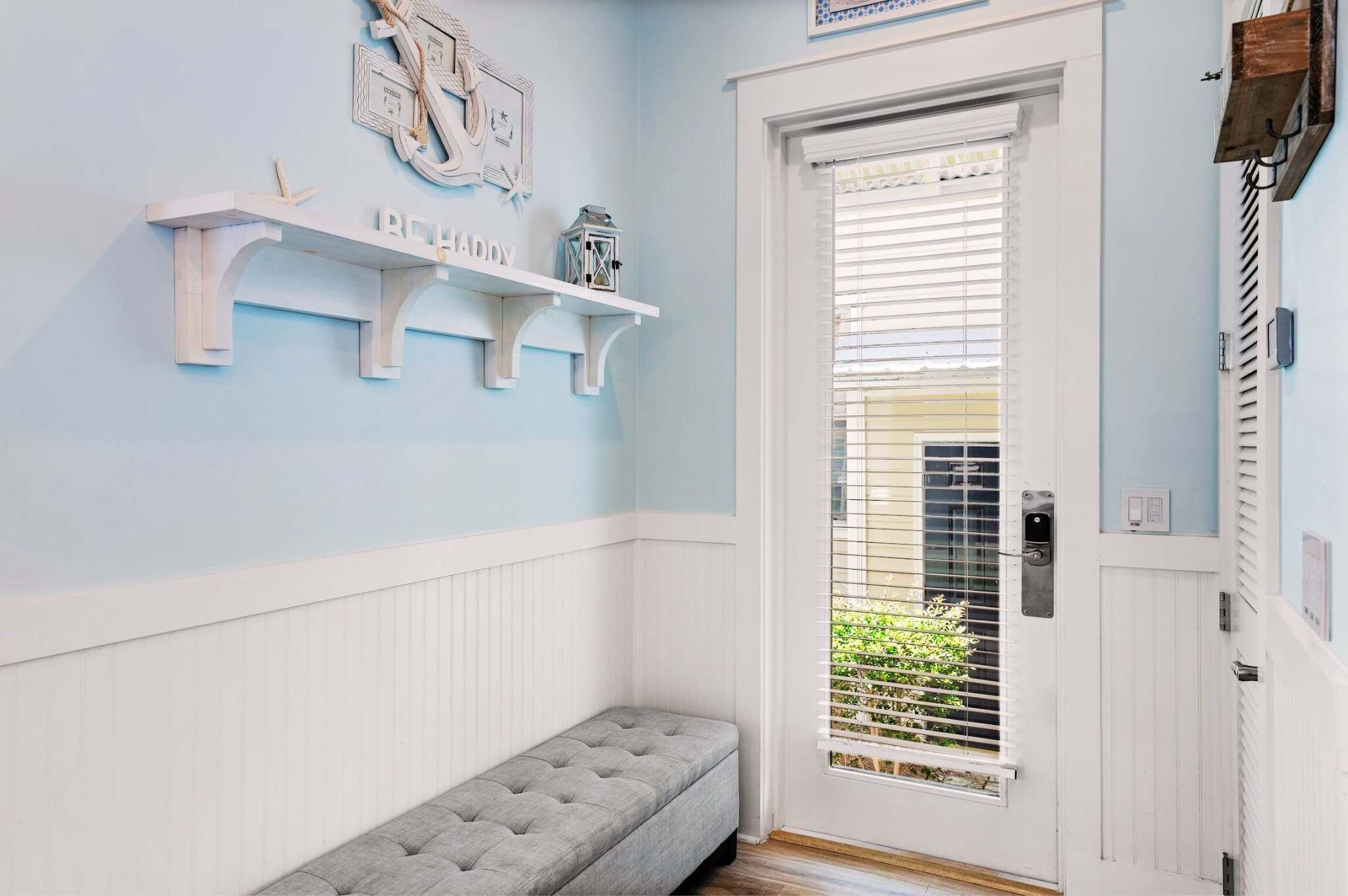 A room with a bench, a door with a window, and a wall-mounted shelf with decorative items.