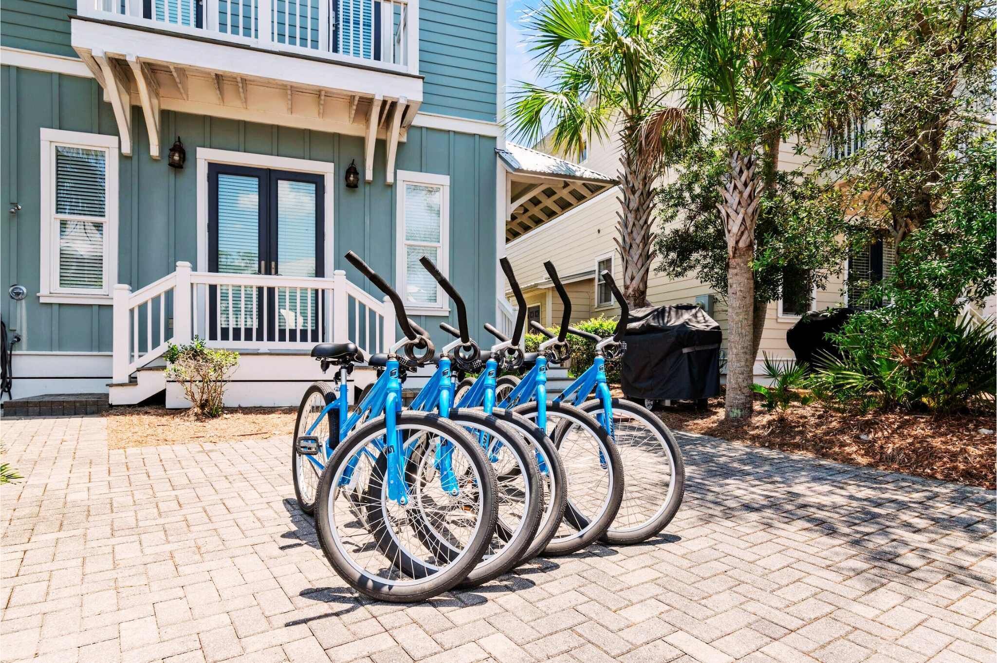 Een rij blauwe fietsen geparkeerd voor een gebouw met een veranda en een palmboom in de buurt.