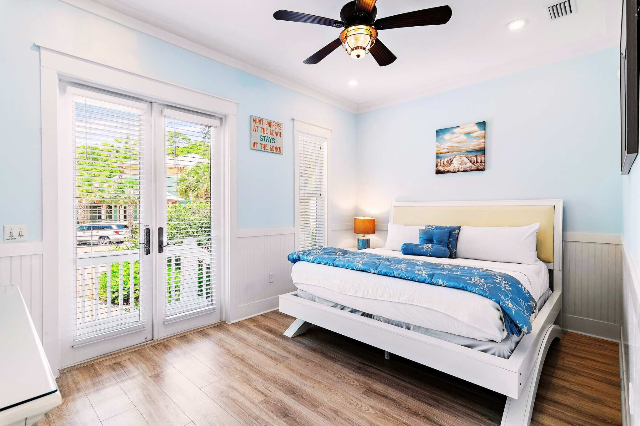 Un dormitorio con cama, ventilador de techo, ventana con persianas y una puerta.