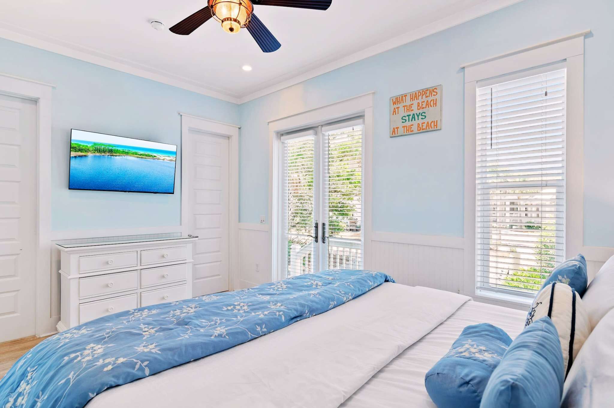 A bedroom with a bed, a TV, a ceiling fan, and a window with blinds.