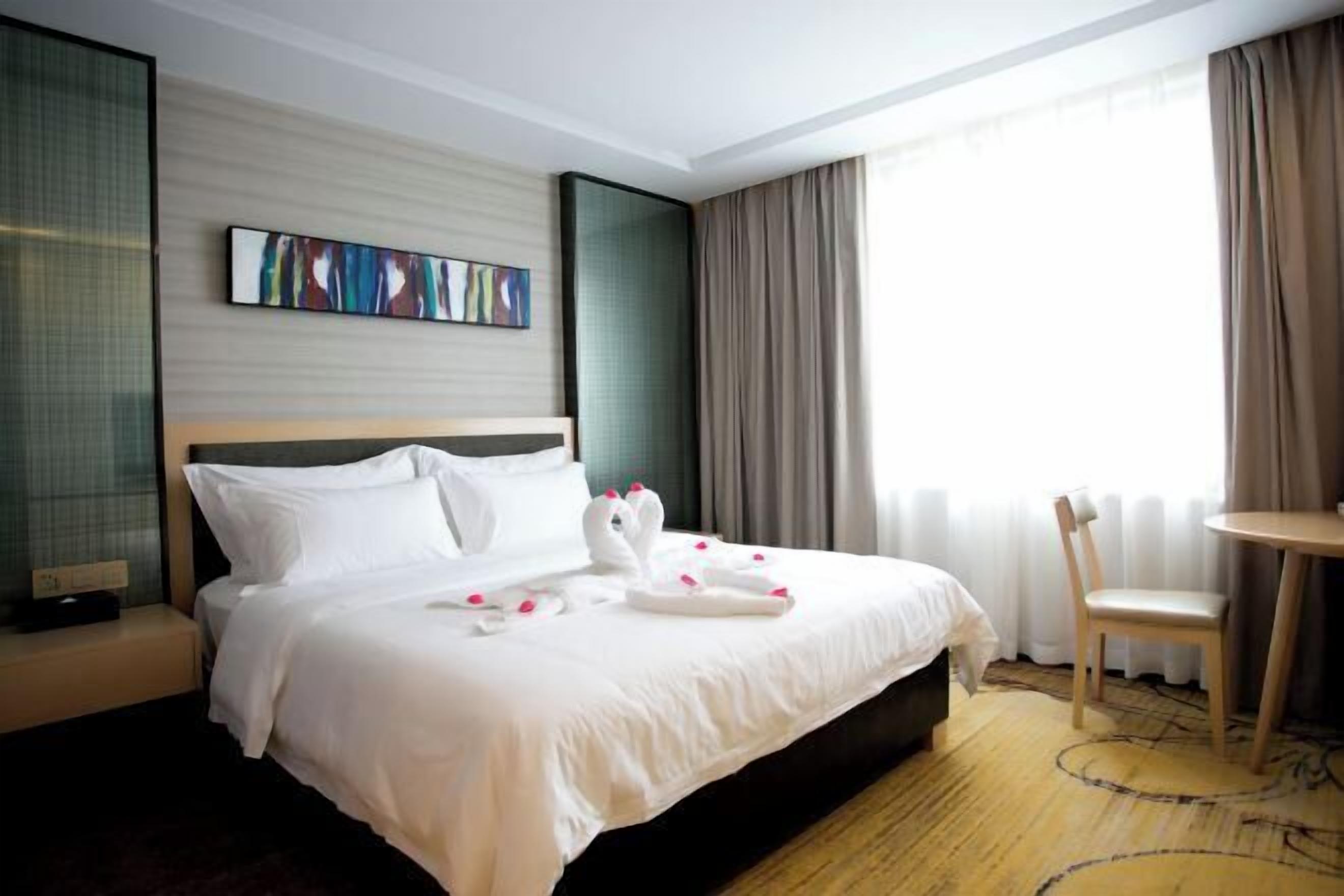 A hotel room with a large bed, a small table, a chair, and a painting on the wall.