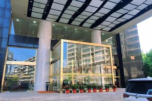 A modern building with a glass facade, large columns, and a vehicle parked in front.