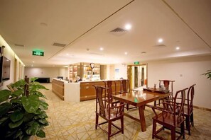 Área de jantar de hotel com mesa central e cadeiras, um balcão de recepção e um piso estampado.