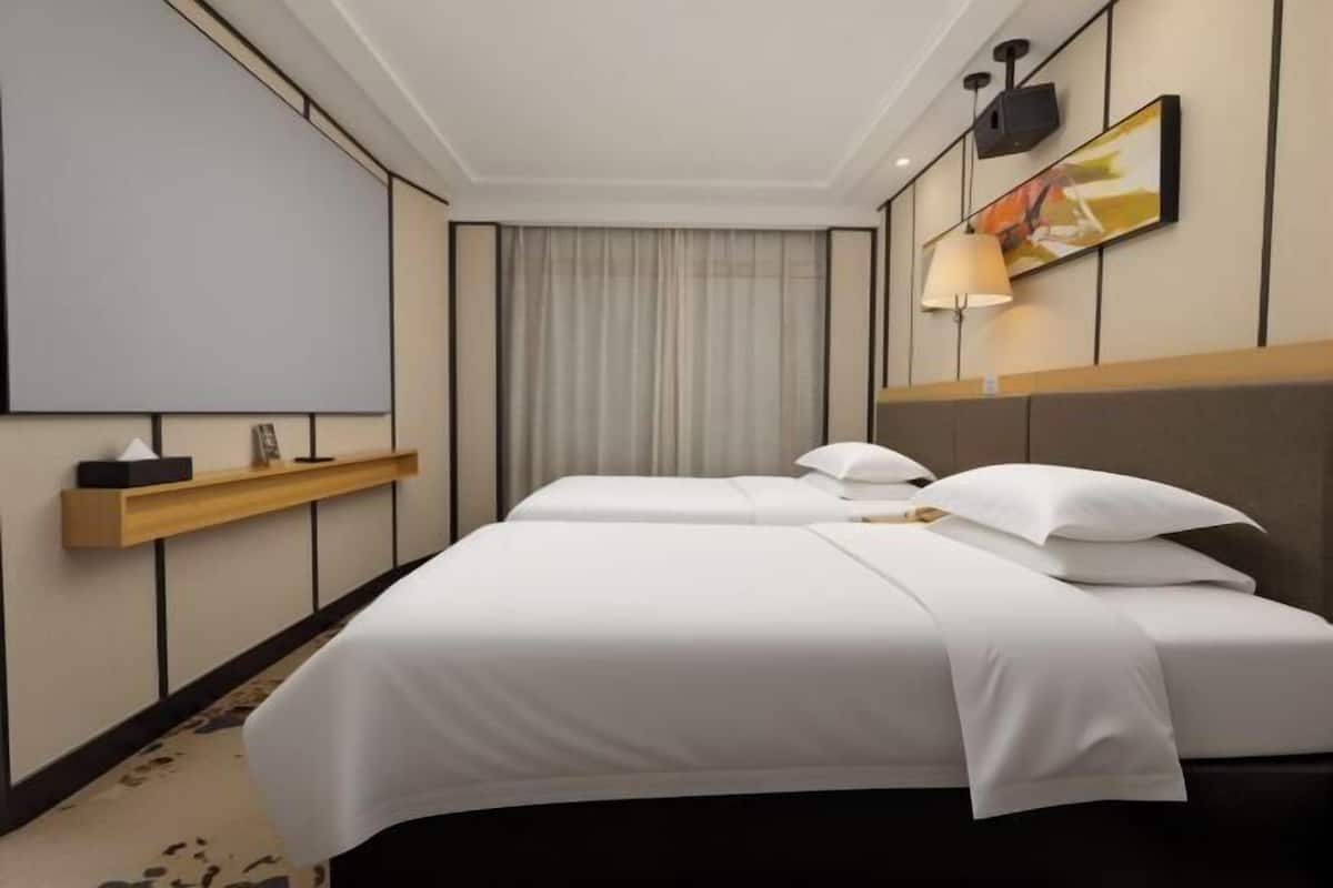 Une chambre d’hôtel avec deux lits, un téléviseur fixé au mur, une lampe de chevet et une fenêtre avec des rideaux.