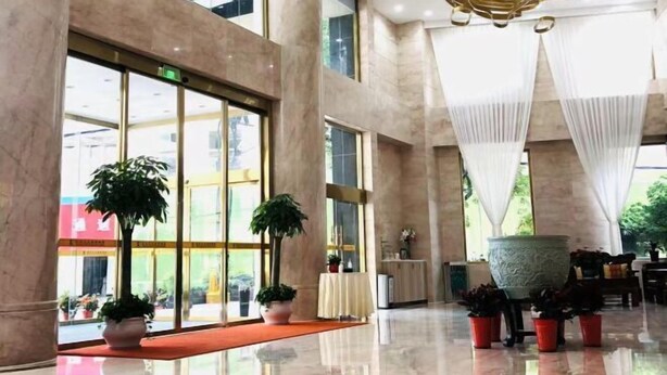 Un hall d’entrée spacieux, doté de grandes fenêtres, de colonnes en marbre et de plantes en pot.