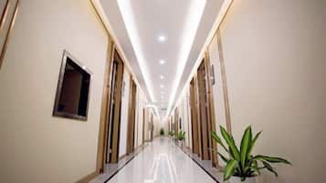 Pasillo de hotel con piso reflectante, puertas a ambos lados y plantas en macetas.