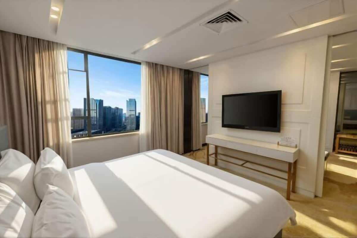 Une chambre d’hôtel avec un grand lit, un téléviseur fixé au mur et une vue sur la ville par la fenêtre.