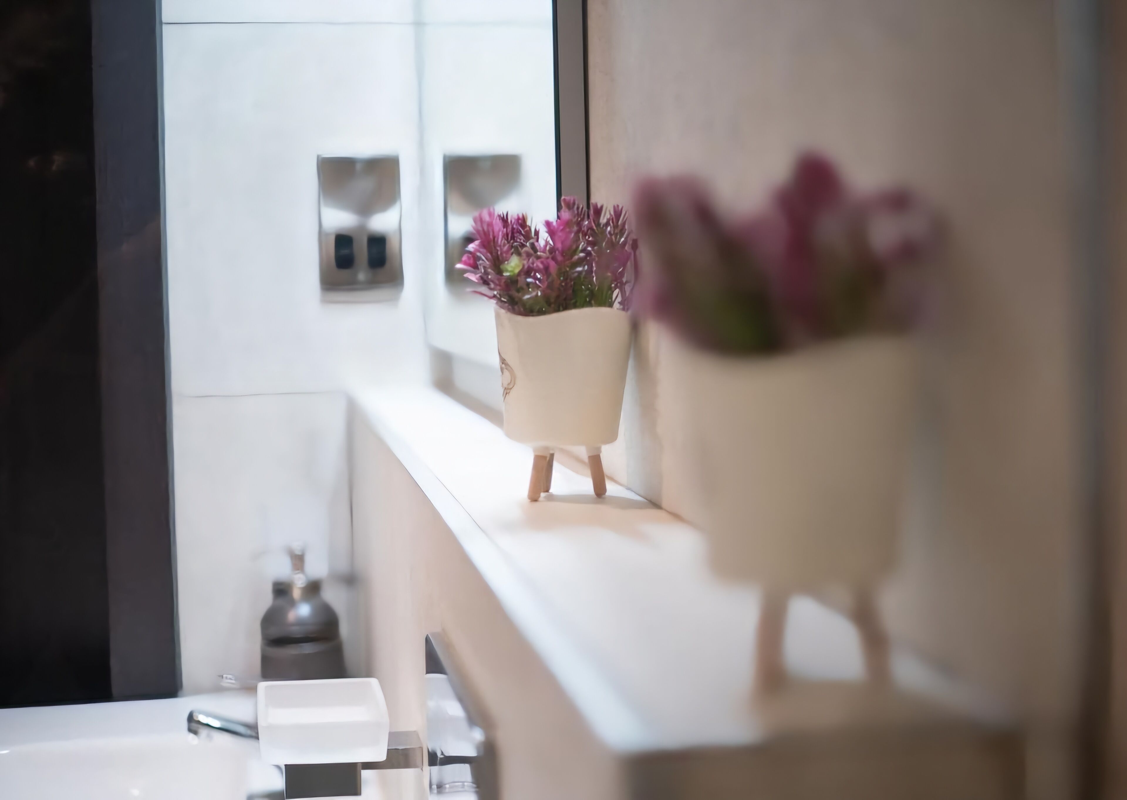 Une salle de bain moderne avec un meuble-lavabo blanc, un miroir et deux plantes en pot posées sur le plan de travail.