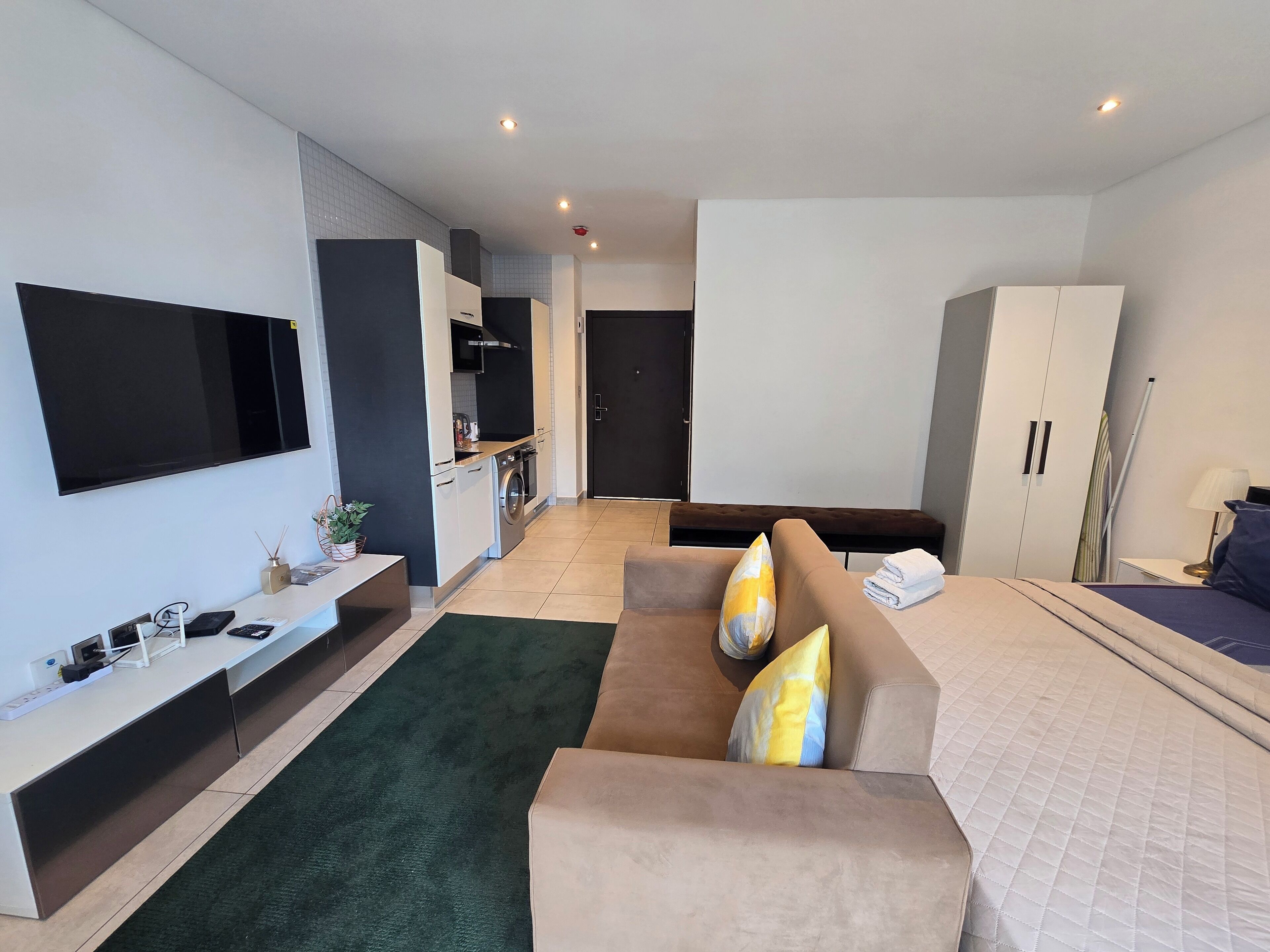 Ein modernes Hotelzimmer mit einer Schlafcouch, einem Bett, einem Fernseher, einer Küchenzeile und einem Kleiderschrank.