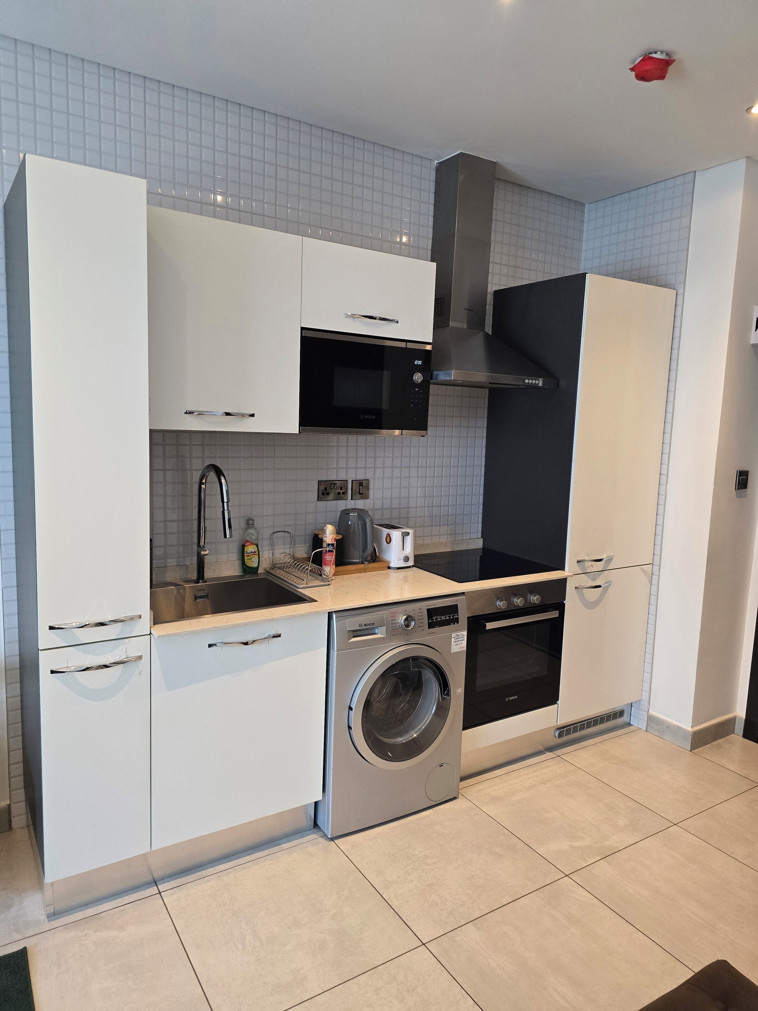 A compact kitchen with white cabinets, a Bosch microwave, a built-in oven, and a front-loading washing machine.