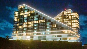 A multi-story hotel with a modern design, featuring balconies and illuminated windows.