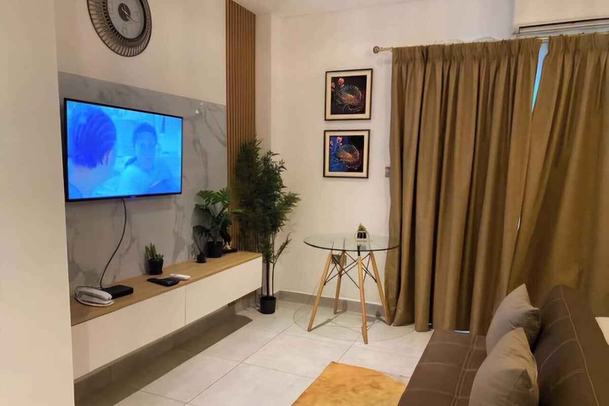 Ein modernes Wohnzimmer mit Flachbildfernseher, einem Glastisch, einem braunen Sofa und einem kleinen Beistelltisch mit Pflanze.