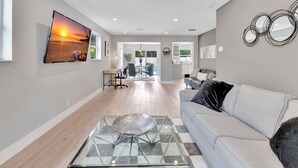 A modern living room with a sofa, a glass coffee table, and a large TV displaying a sunset scene.