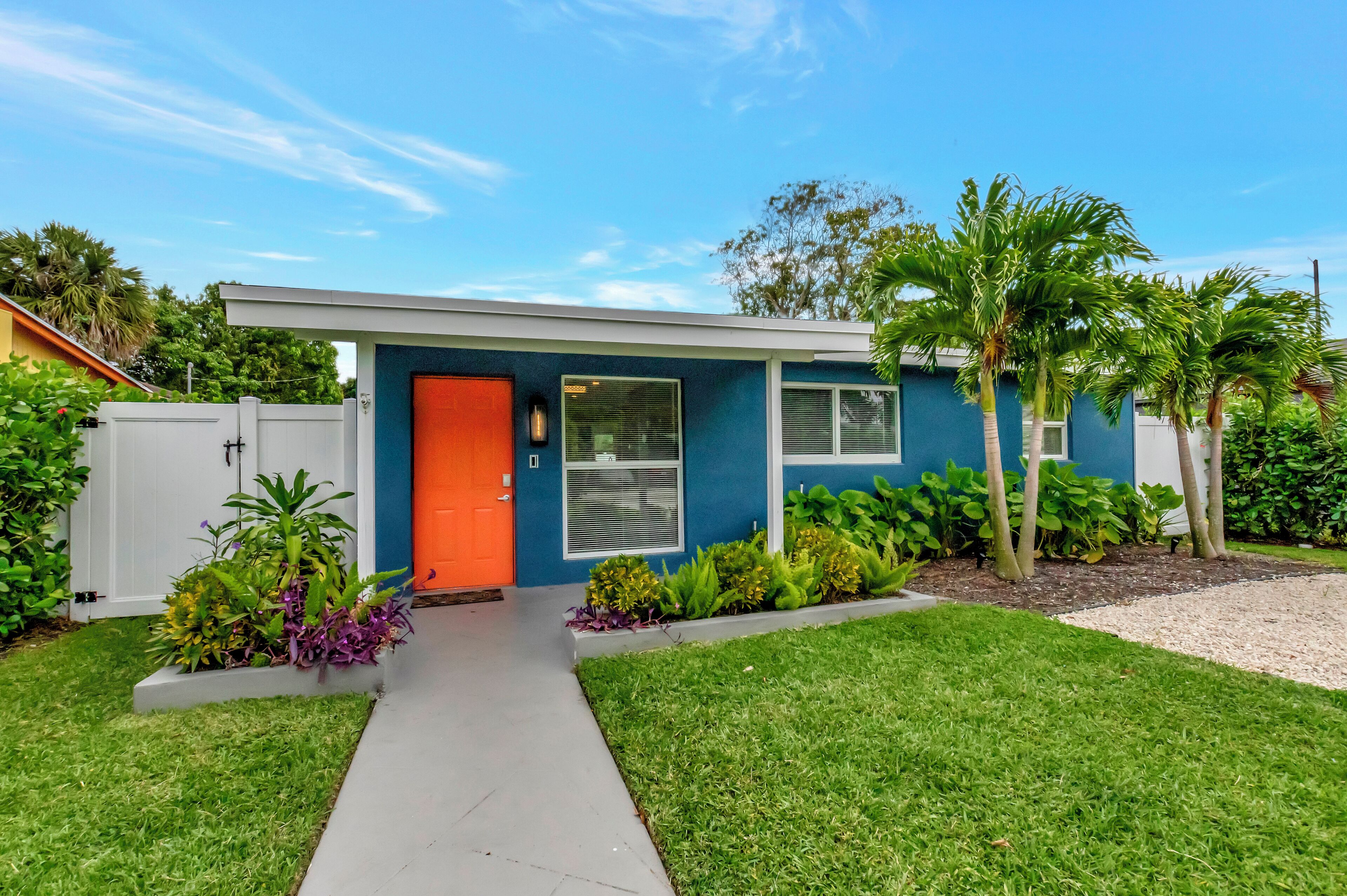 A modern house with a blue exterior, an orange door, and a well-maintained lawn with various plants.