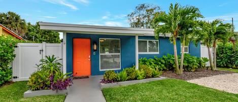 A modern house with a blue exterior, an orange door, and a well-maintained lawn with various plants.