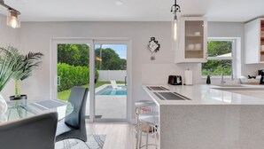 A modern kitchen with a glass dining table, bar stools, and a view of a swimming pool.