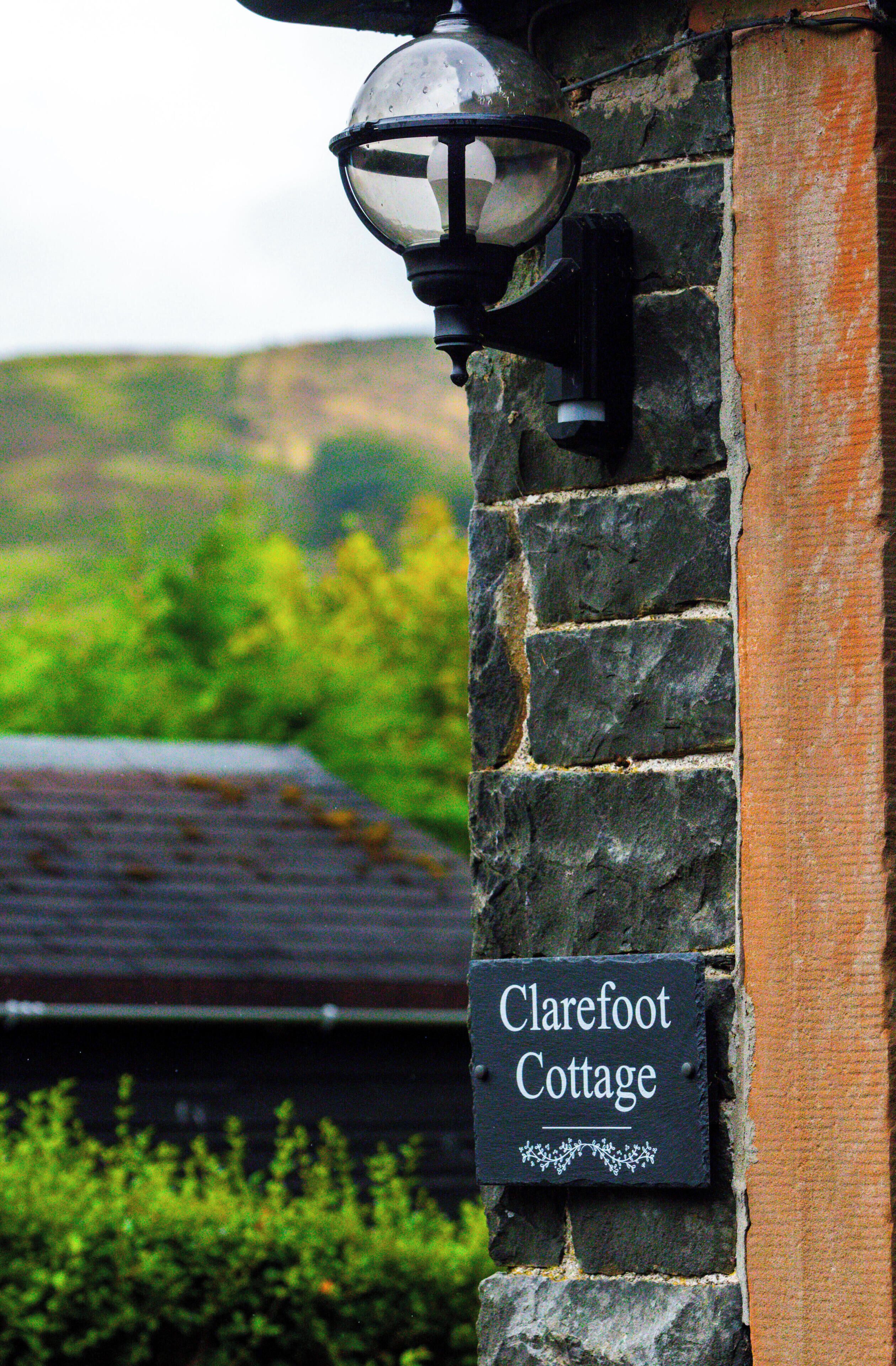 A sign reading "Clarefoot Cottage" mounted on a stone wall with a lantern above it.