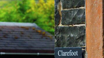 A sign reading "Clarefoot Cottage" mounted on a stone wall with a lantern above it.