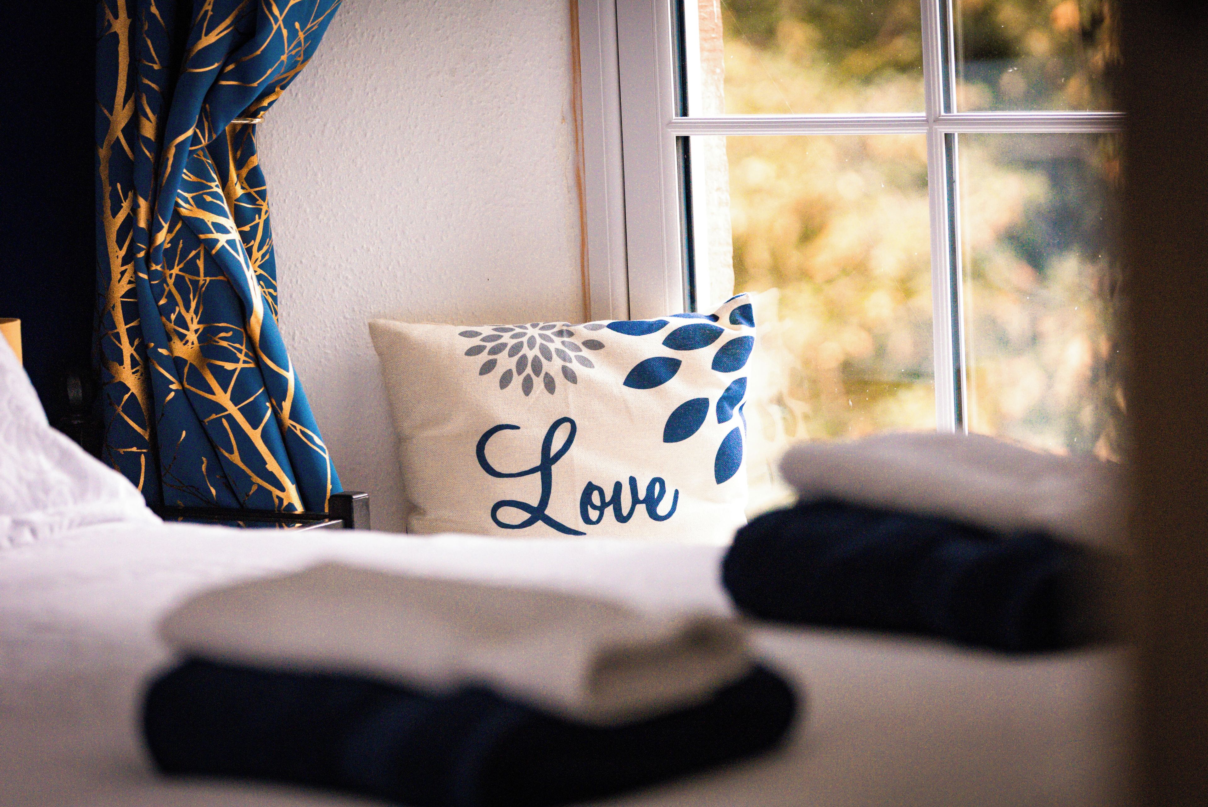 A bed with a pillow that has a leaf pattern and the word 'Love' on it.