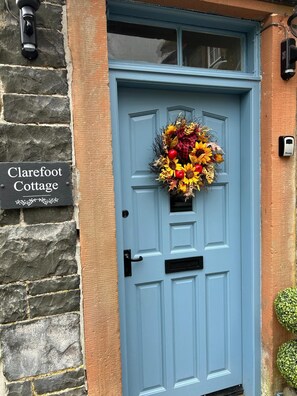 A blue door with a wreath, a stone wall, and a sign reading "Clarefoot Cottage".