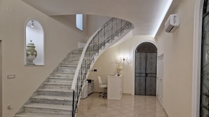 A marble staircase with a curved design, leading to a door with a decorative metal gate. - Villa Esmeralda (Salerno)